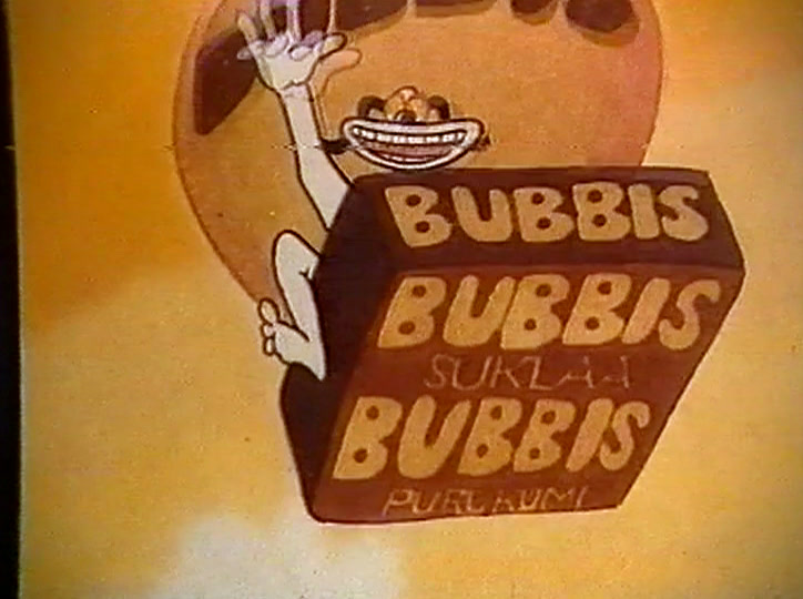 He holds up a brown pack reading BUBBIS SUKLAA BUBBIS PURUKUMI.