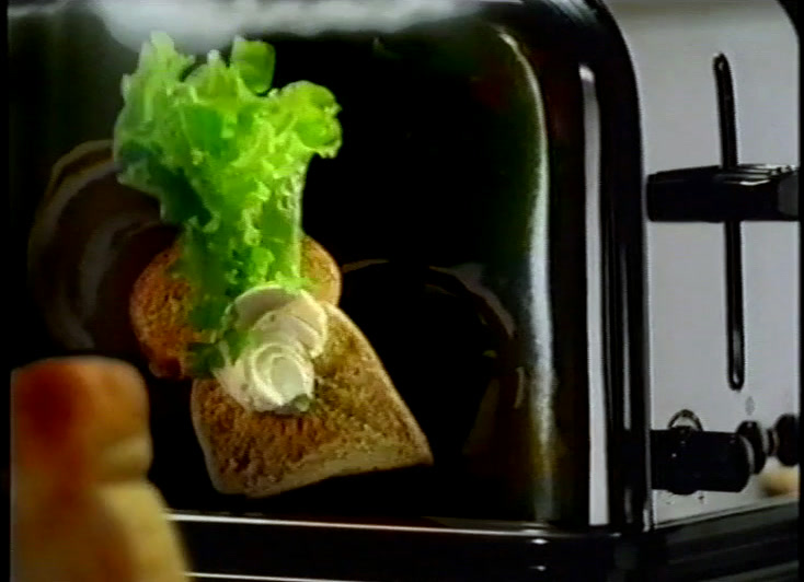 The dressed slice tips forward out of the slot, the lettuce leaf catching the light