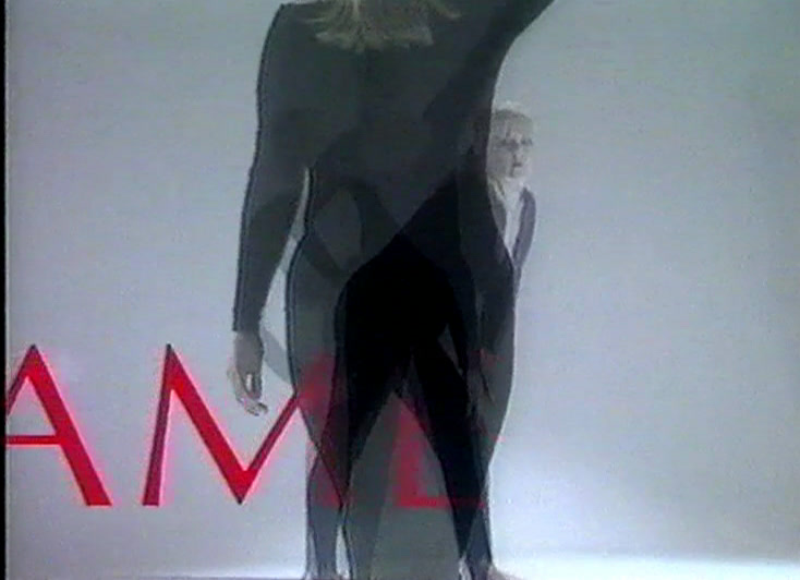 A woman in black crosses a white studio, doubled by a dissolve, red letters behind her