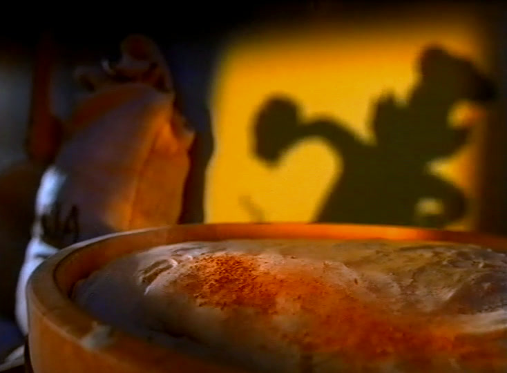 A cartoon baker’s shadow waves on a yellow wall above a loaf proving in a bowl