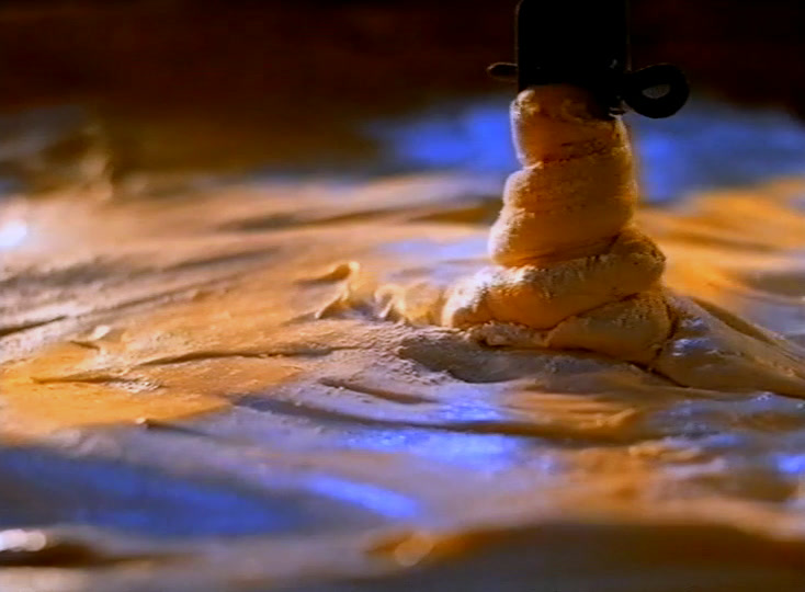 Dough turns under a mixing hook on a floured bench, lit low and warm