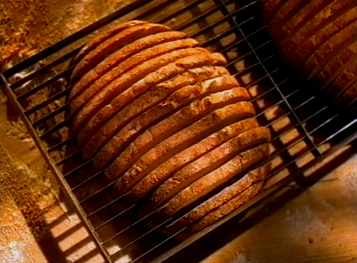 Round slashed loaves cool on a wire rack above a dark oven