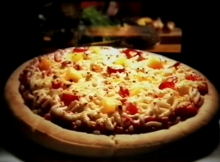 The baked pizza on a dark counter, browned cheese with yellow and red pieces