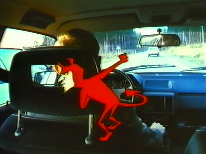 The devil sprawls across the dashboard and wheel while the driver’s hand grips the rim.