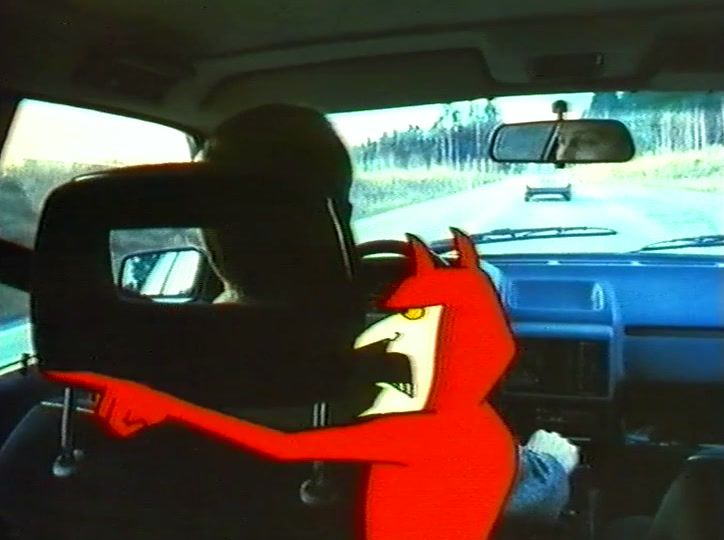 A drawn red devil with horns stands on the front seat of a moving car, road ahead.