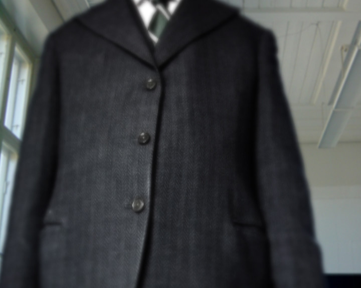 A blurred dark grey jacket over a white shirt and dark tie, cropped above the collar.