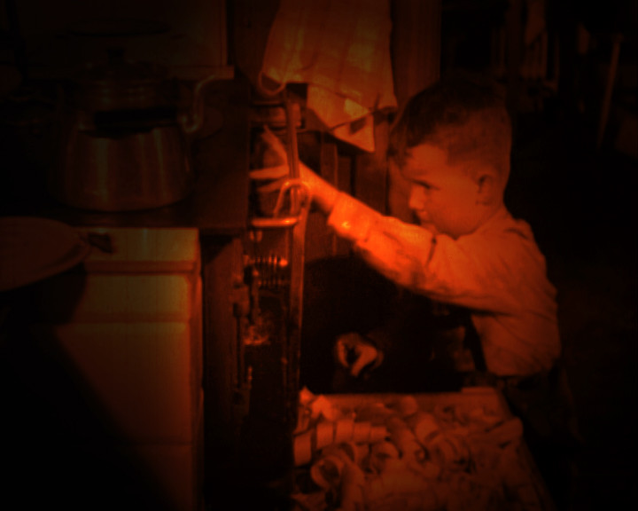 A small boy in a white shirt reaches into the open door of a glowing stove.