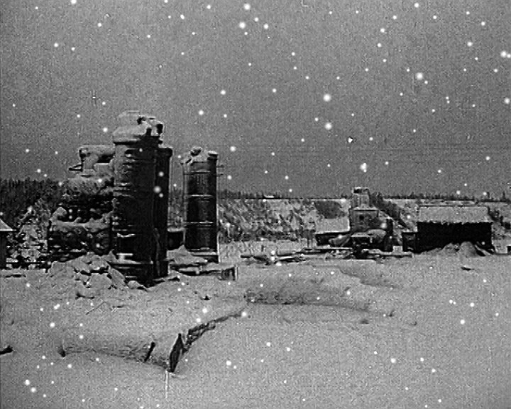 Brick chimneys stand among snow-covered rubble of a destroyed building, snow falling across the frame.