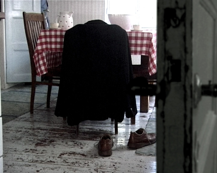A dark coat hangs over a chair at a red checked table, brown shoes on the floor.