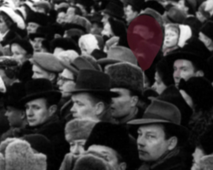 A dense crowd in winter hats and coats, with one dark red balloon among the heads.
