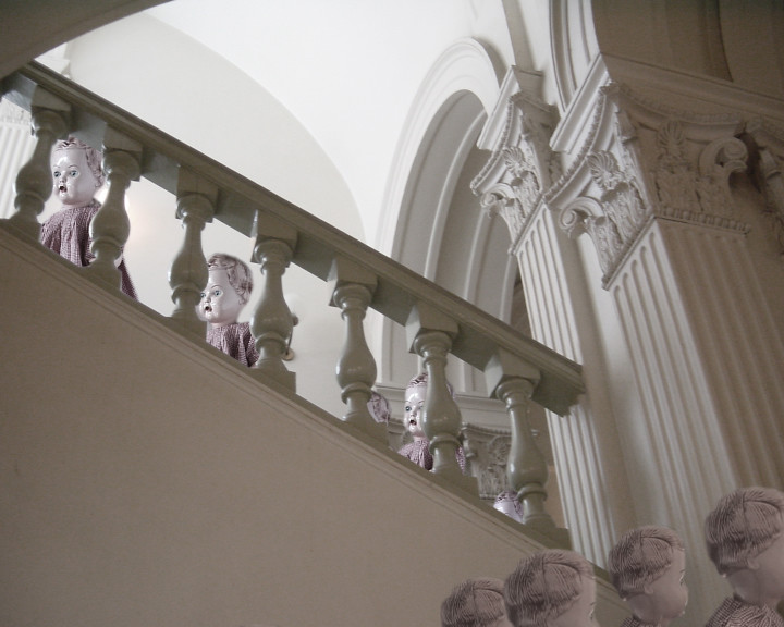 Doll heads with open mouths sit along a pale stone balustrade in a classical stair hall.