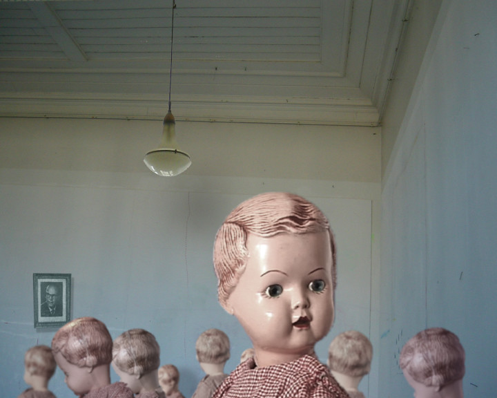 Doll heads fill a pale blue room under a pendant lamp, a framed portrait on the wall.