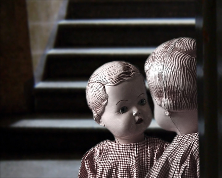 Two dolls in checked dresses stand at the foot of a dim stone staircase.
