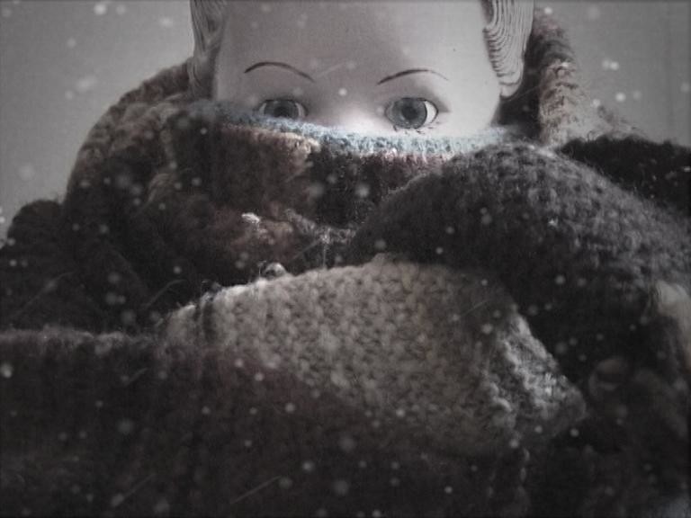 A face above thick knitted woollens, only the eyes and eyebrows showing, snow falling around it.