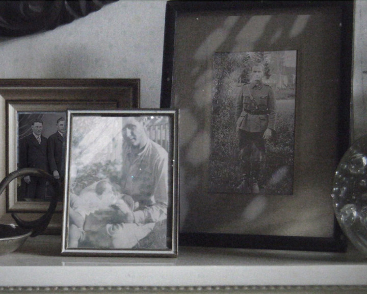 Framed black and white photographs on a mantelpiece: a man in uniform, a man holding a baby.