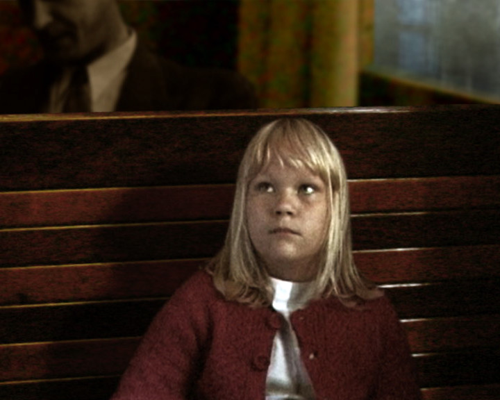 A girl in a red cardigan sits on a wooden bench, looking up and away.