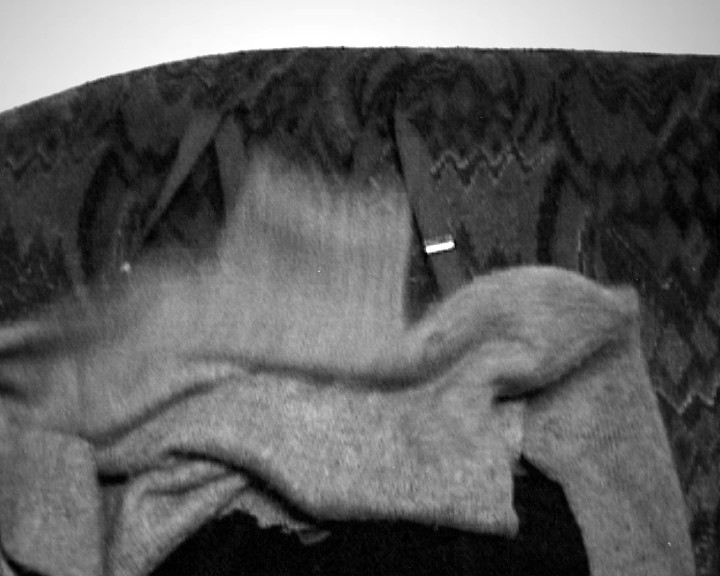 A grey knitted garment lies crumpled on a dark patterned sofa, seen very close.