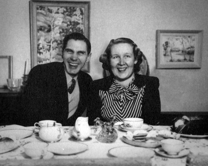A man and a woman laugh together behind a laid table of coffee cups and pastries.