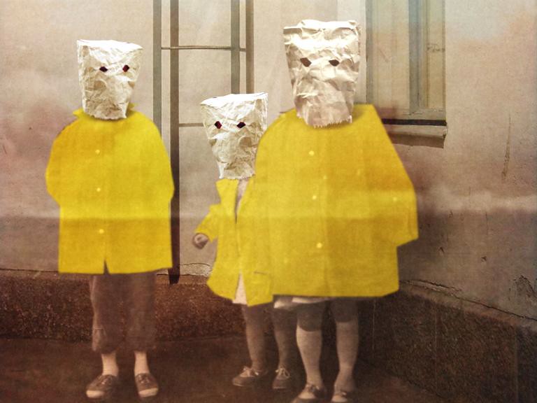 Three figures stand against a wall wearing paper bags over their heads and bright yellow coats.
