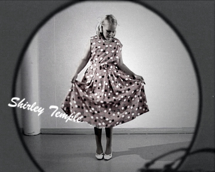 A girl holds out the skirt of a polka-dot dress inside an oval frame, captioned “Shirley Temple”.