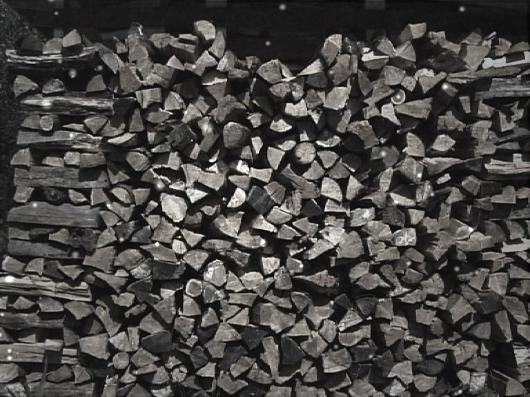 A wall of split firewood stacked end on, with snowflakes falling in front of it.