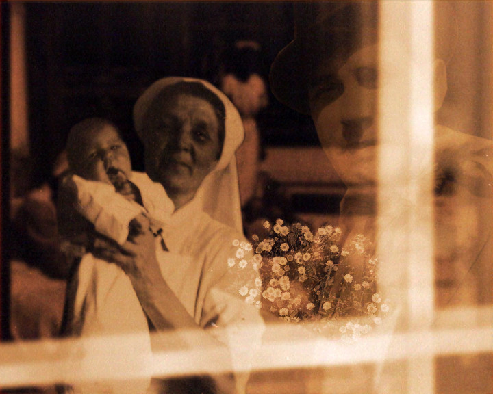 A woman in a white headdress holds a newborn baby, daisies and a faint second face superimposed.