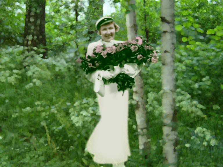 A cut-out photograph of a woman in a white dress and cap holding roses among birches.