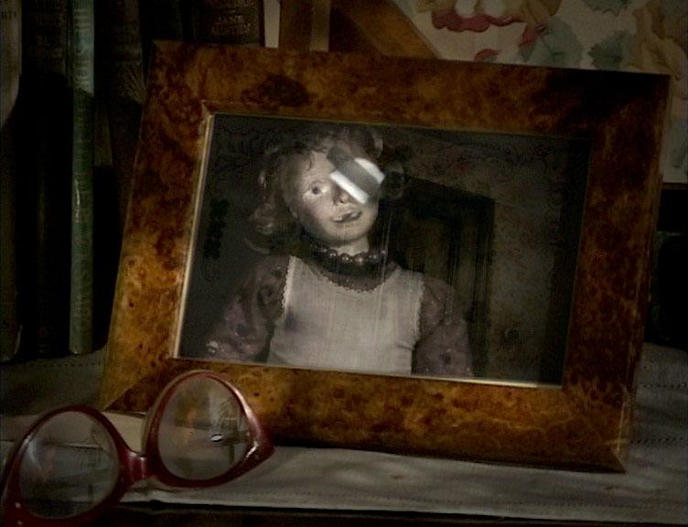 A framed photograph of a girl stands on a shelf, her eyes scratched white, red spectacles in front.
