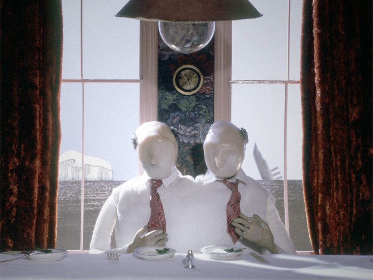 Two bald figures with blank faces, in white shirts and pink ties, at a table by a window.