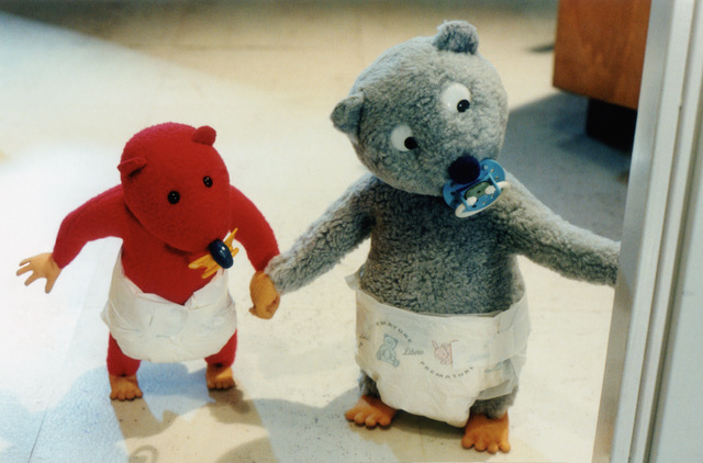 Still from Urpo and Turpo, Turpo the red bear and Urpo the grey bear standing side by side in their nappies, holding hands, a dummy in Urpo's mouth