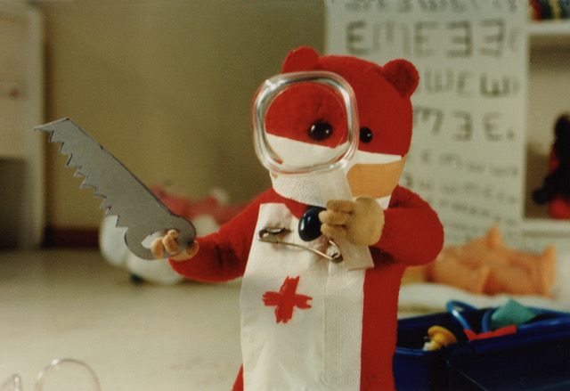Still from Urpo and Turpo, Turpo the red bear in a surgeon's mask and apron, holding up a toy saw